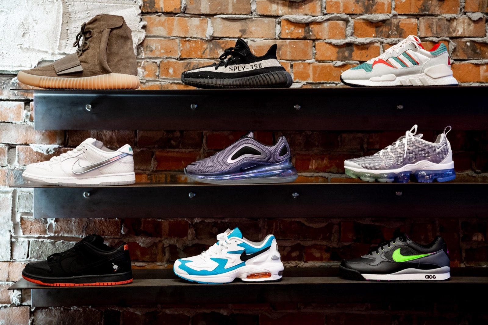 Sneakers including Adidas and Nike models displayed on shelves against an exposed brick wall.