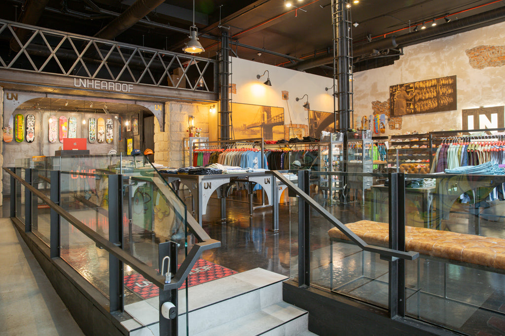Wide view of the multi-level Unheardof store interior, with a large historic bridge photograph, a sneaker wall and clothing racks below a mezzanine.