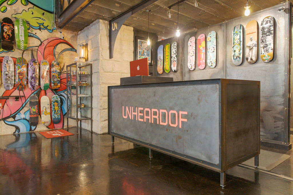 The illuminated Unheardof checkout counter sign in front of a colorful mural and a full wall of skateboard decks.